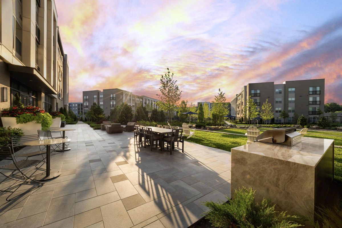Modern courtyard with tables, chairs, and greenery, under a colorful sunset sky.