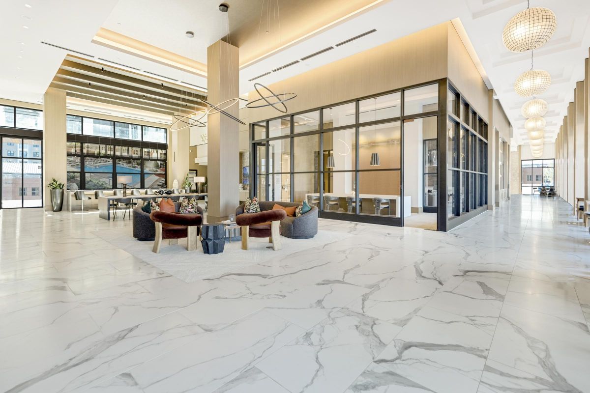 Modern lobby with marble floors, glass-walled meeting room, cozy seating area, and decorative lighting fixtures.