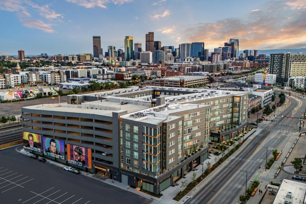 Aerial view of a modern building with murals, set against a city skyline under a partly cloudy sky.