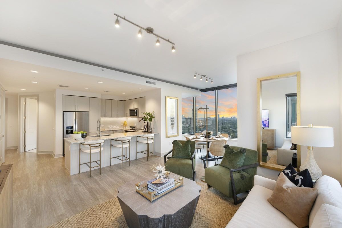 Modern open-plan living room and kitchen with large windows, contemporary furniture, and a sunset view.