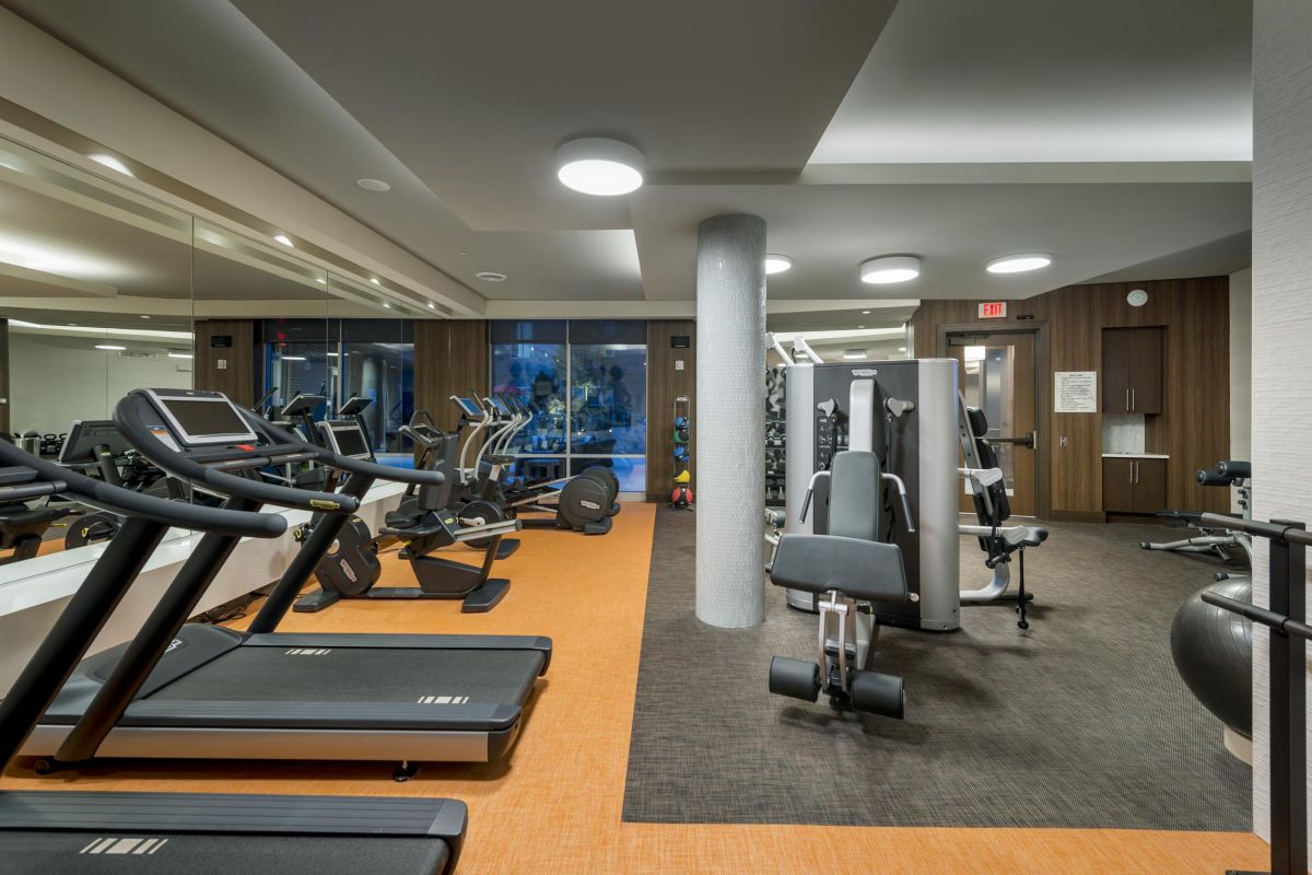 Modern gym with treadmills, weight machines, free weights, and an exercise ball on an orange and brown floor.