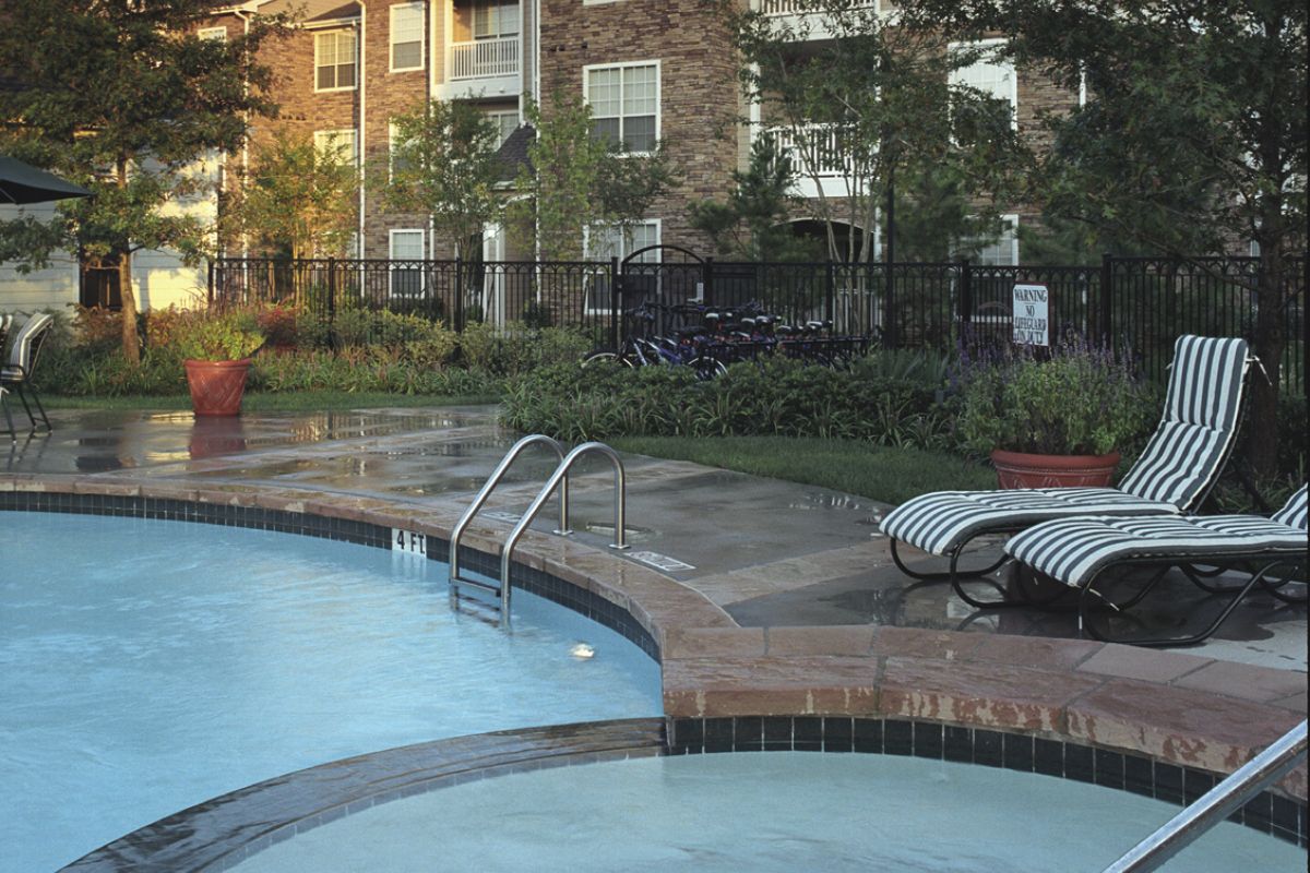 Hot tub and pool with lounge chairs in front of a brick apartment building at sunset.