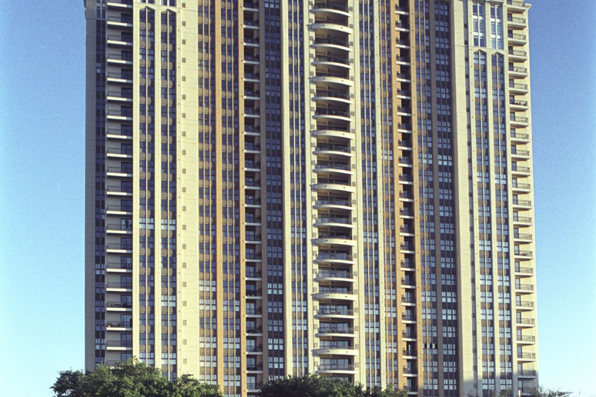 Tall modern apartment building at 1200 Post Oak with many windows, trees in front, and a red convertible car driving by.