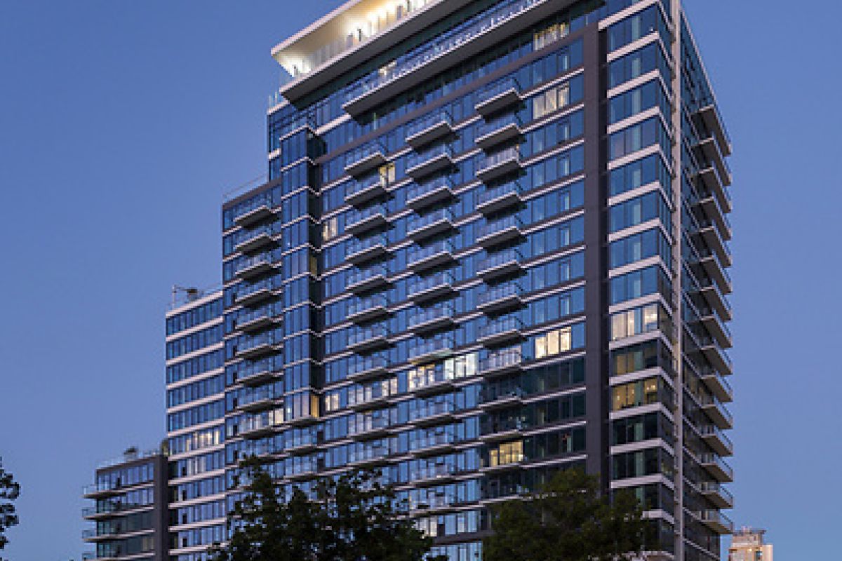 Modern high-rise apartment building at dusk with glowing lights and blurred car trails in the foreground.