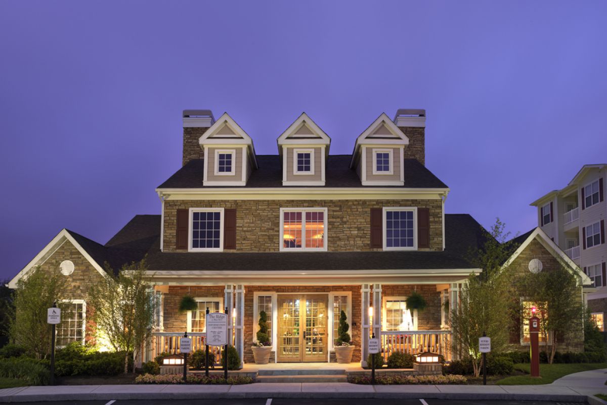 A large, well-lit suburban house with three dormer windows and a front porch at dusk.