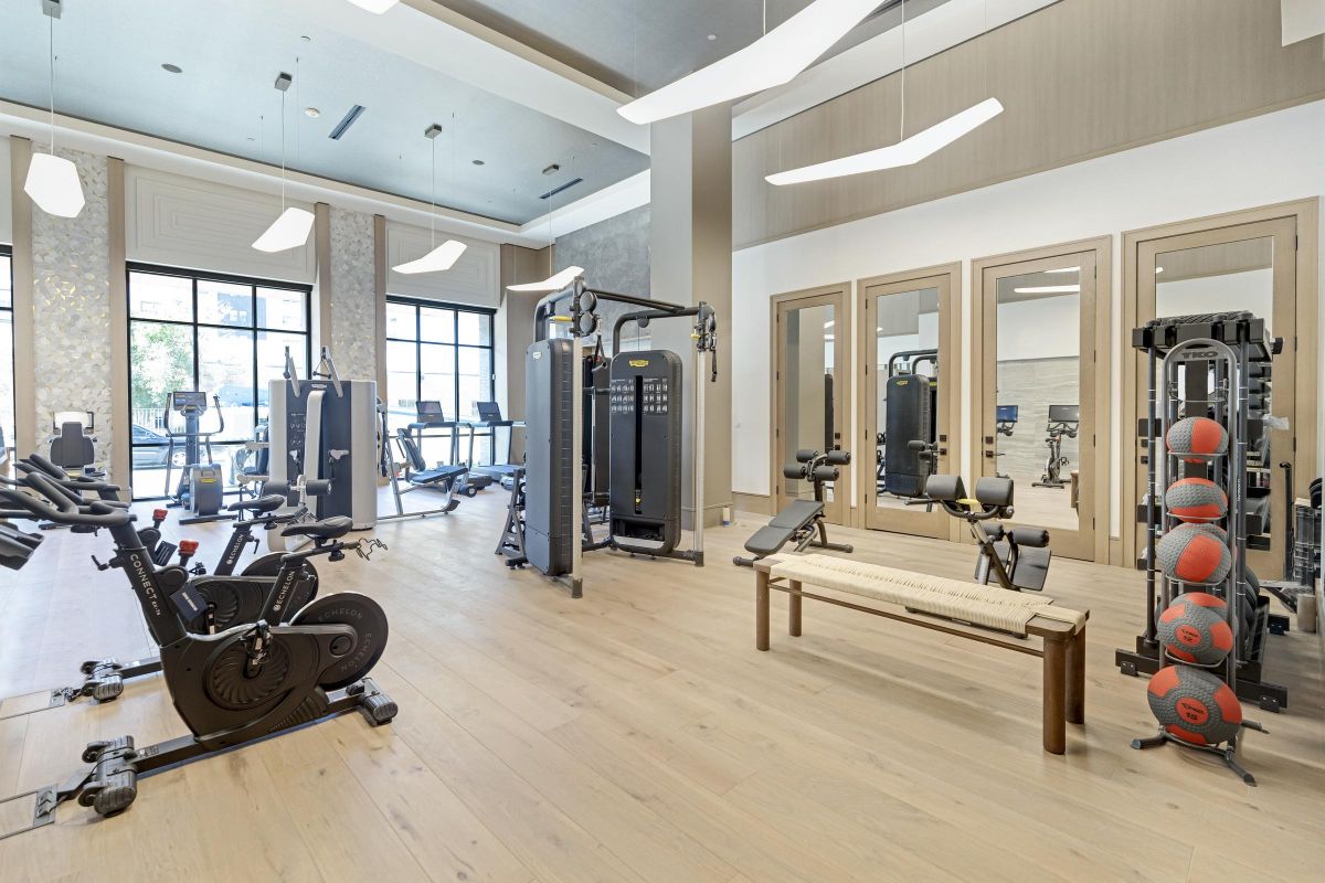 Spacious gym with exercise bikes, weight machines, mirrors, a wooden bench, and medicine balls on a rack.