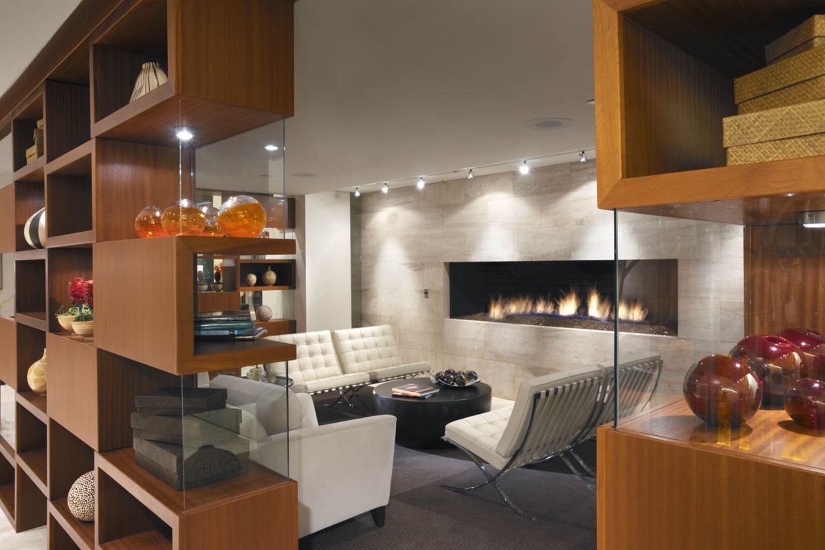 Modern living room with beige sofas, a long fireplace, and wooden shelving with decorative items.