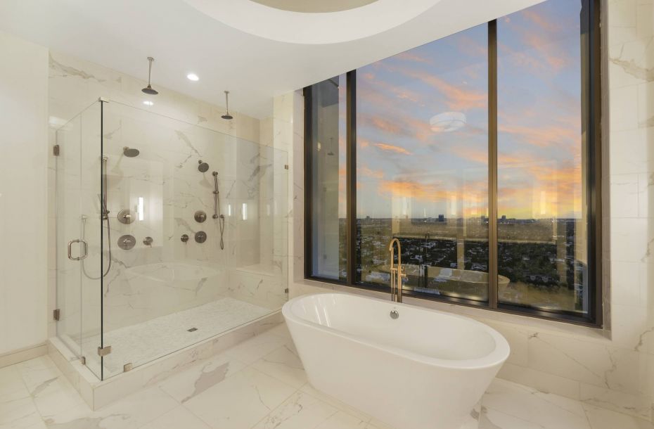 Hanover Company, The Driscoll at River Oaks Luxurious bathroom with a marble shower, freestanding tub, and large window showing a sunset cityscape view.