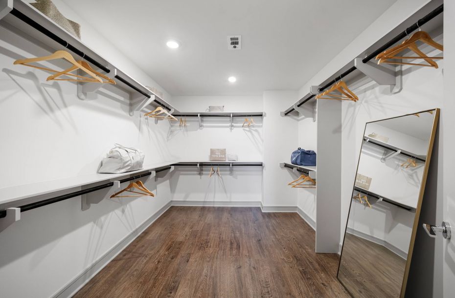 Hanover Company, Hanover Brazos Spacious walk-in closet with wooden floor, hanging rods, empty hangers, and a large mirror on the right wall.