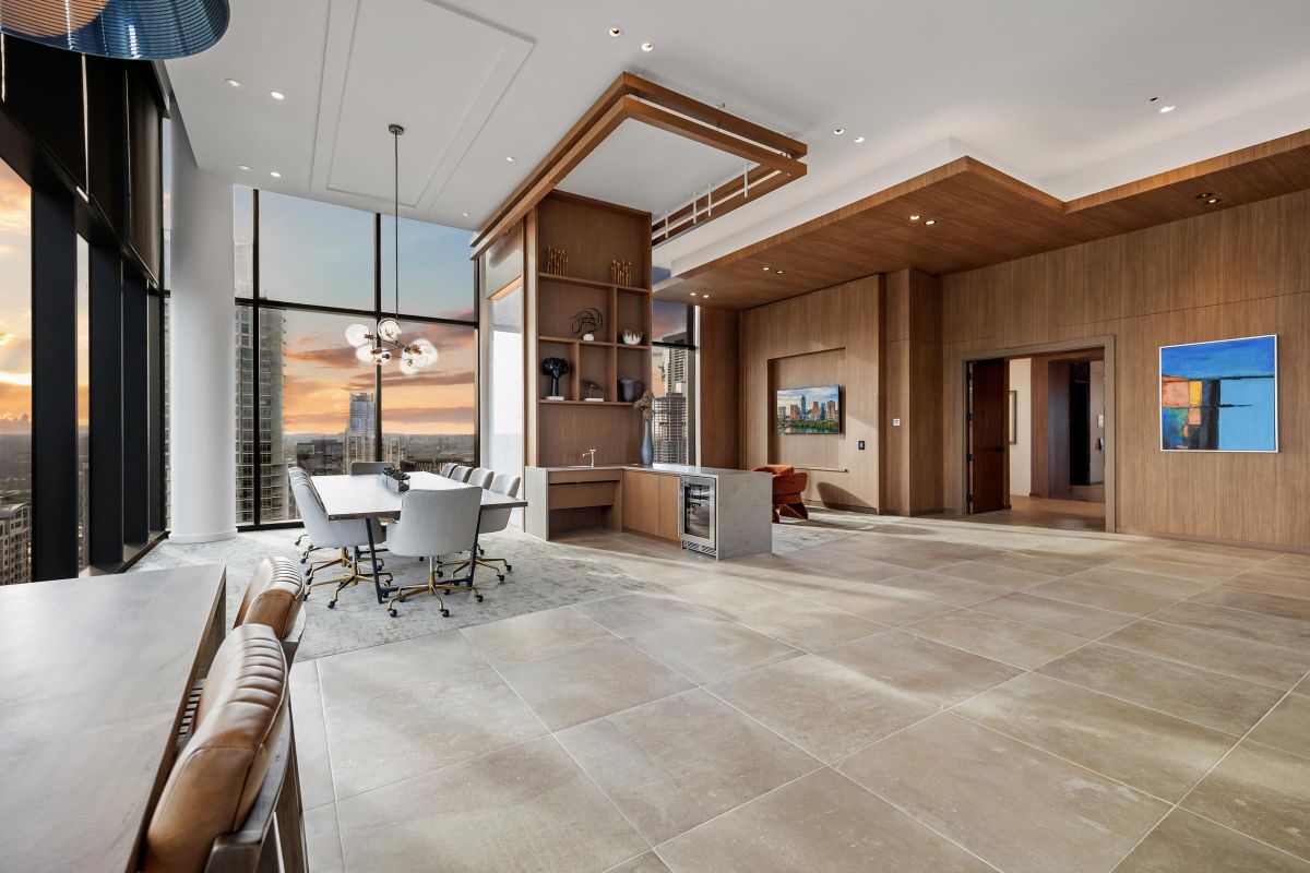 Modern penthouse interior with floor-to-ceiling windows, dining table, and cityscape view at sunset.