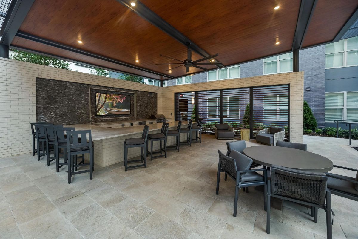 Covered outdoor patio with bar seating, round dining table, lounge chairs, and a wall-mounted TV.
