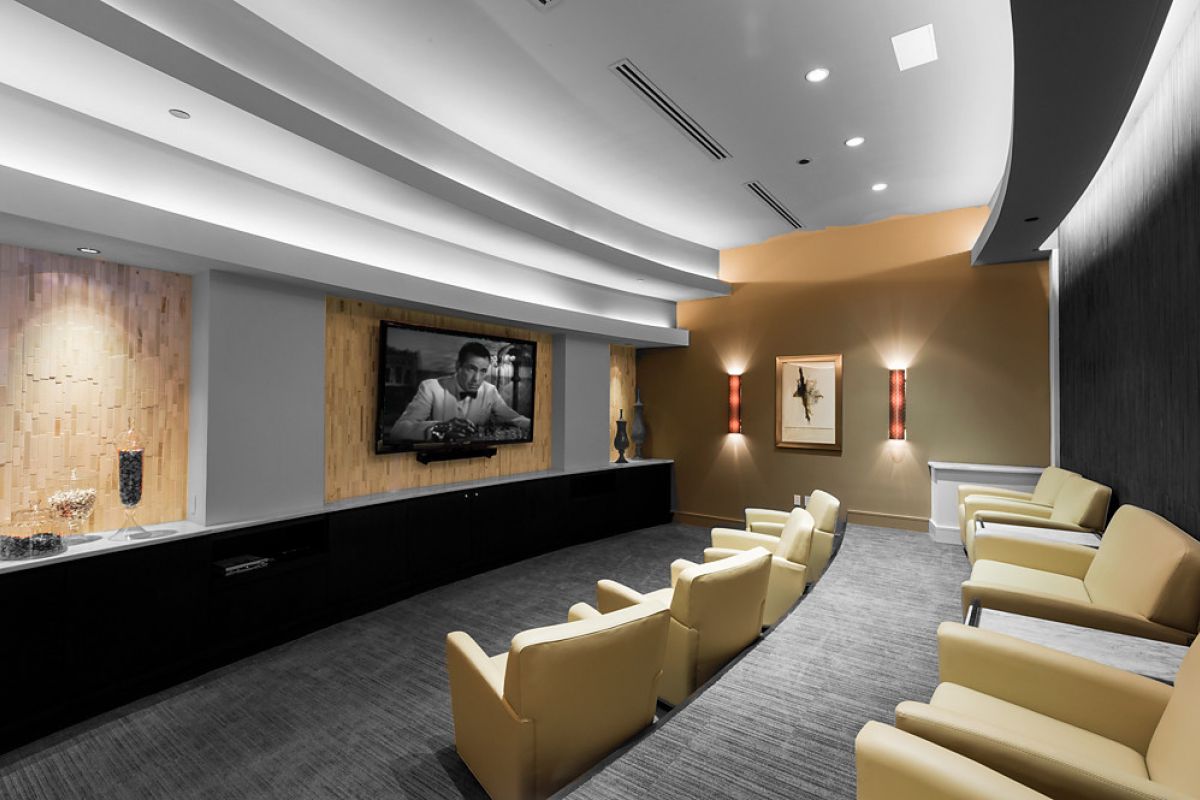 Modern home theater with yellow chairs facing a large TV showing a black and white movie, neutral-toned decor.