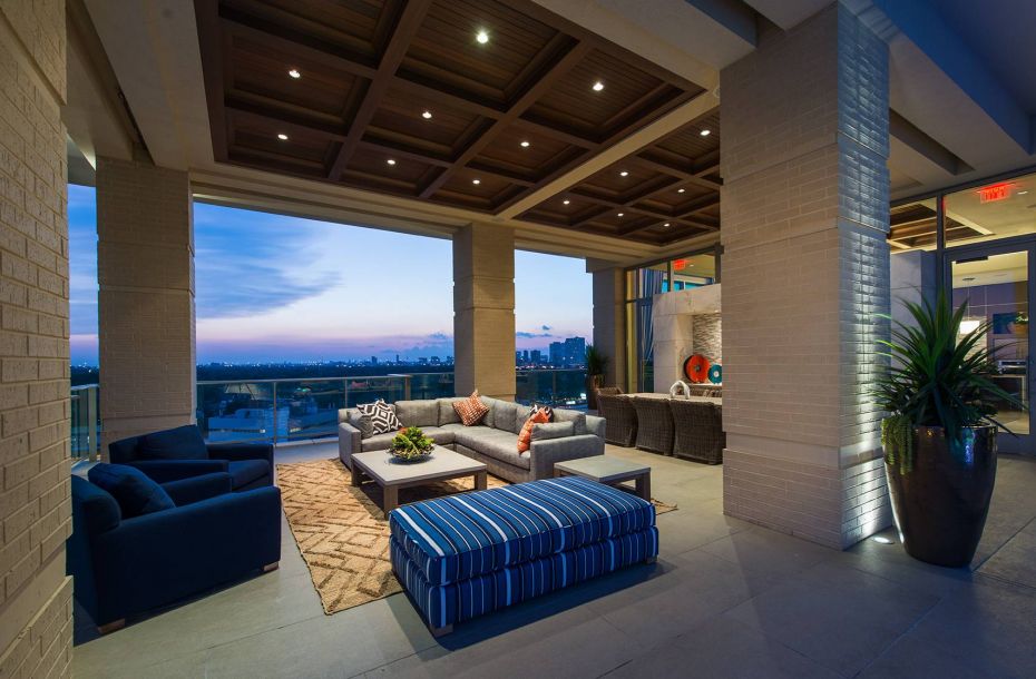Hanover Company, Hanover Southhampton Luxurious rooftop patio with elegant seating, striped ottoman, and city skyline view at dusk.