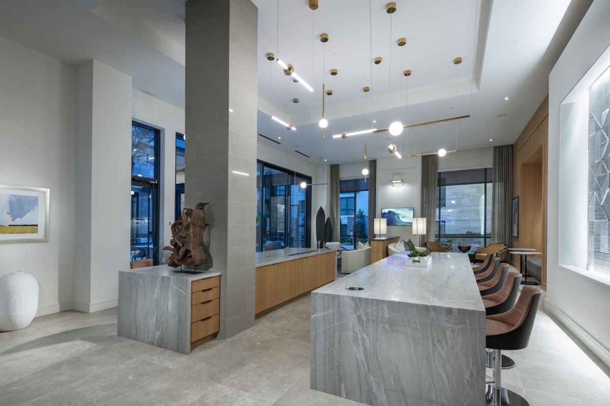 Modern kitchen with marble island, pendant lights, and bar stools. Artwork and large windows enhance the space.
