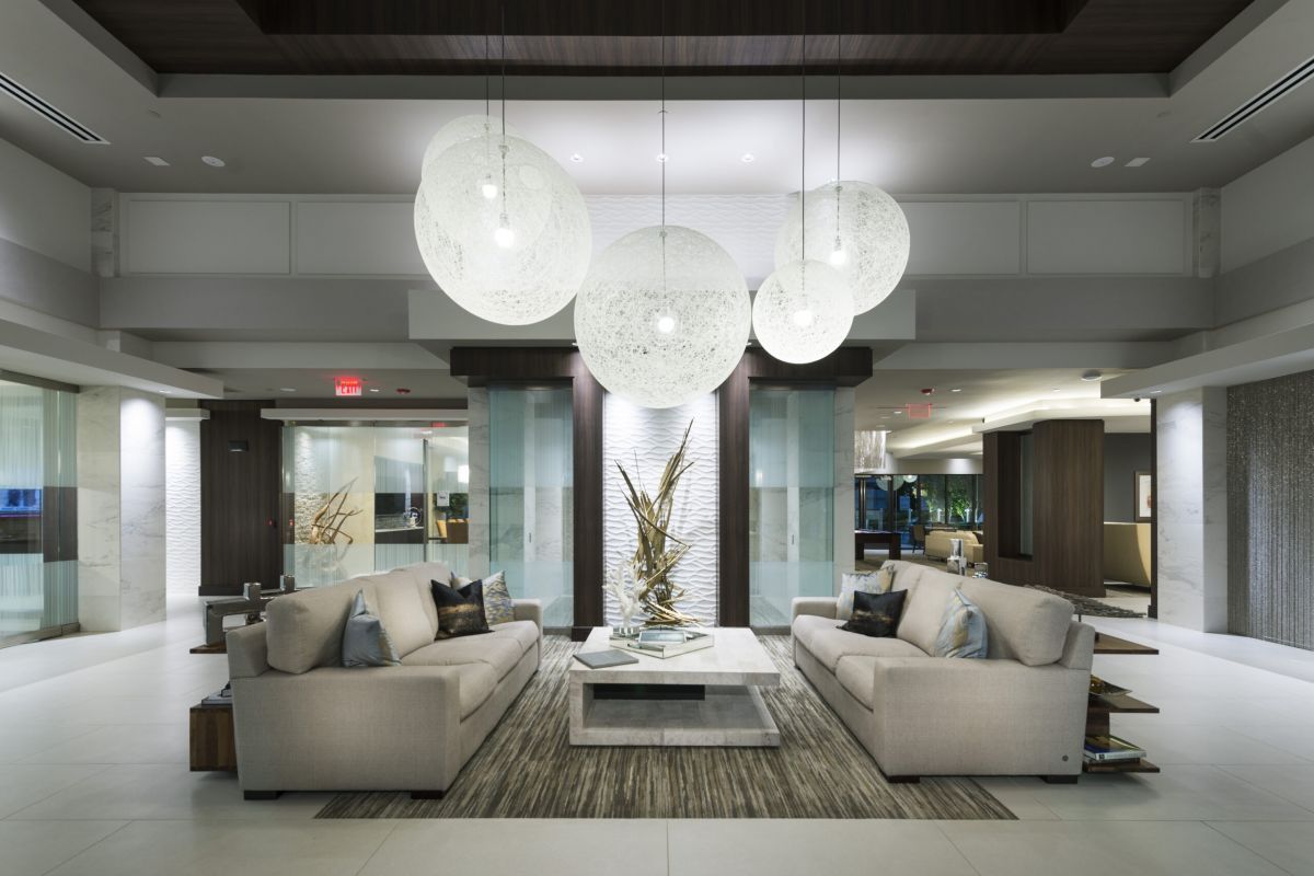 Modern hotel lobby with beige sofas, large globe pendant lights, and a sculptural centerpiece on a low table.