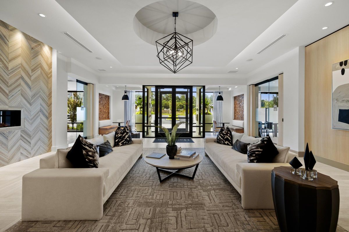 Modern living room with two beige sofas, geometric chandelier, large windows, and abstract art. Bright and spacious.