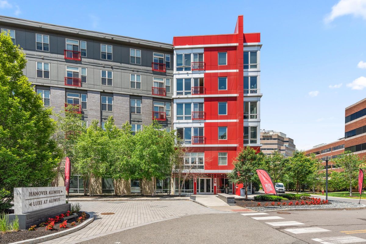 Modern apartment building with red accents, surrounded by trees and a sign reading "Hanover Alewife.