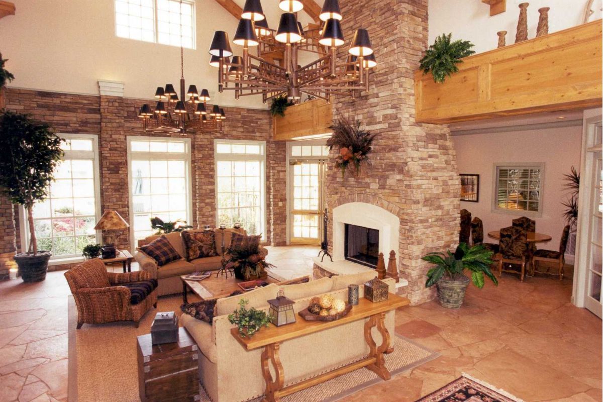 Spacious living room with tall windows, stone fireplace, high ceiling, and comfortable seating arrangement.
