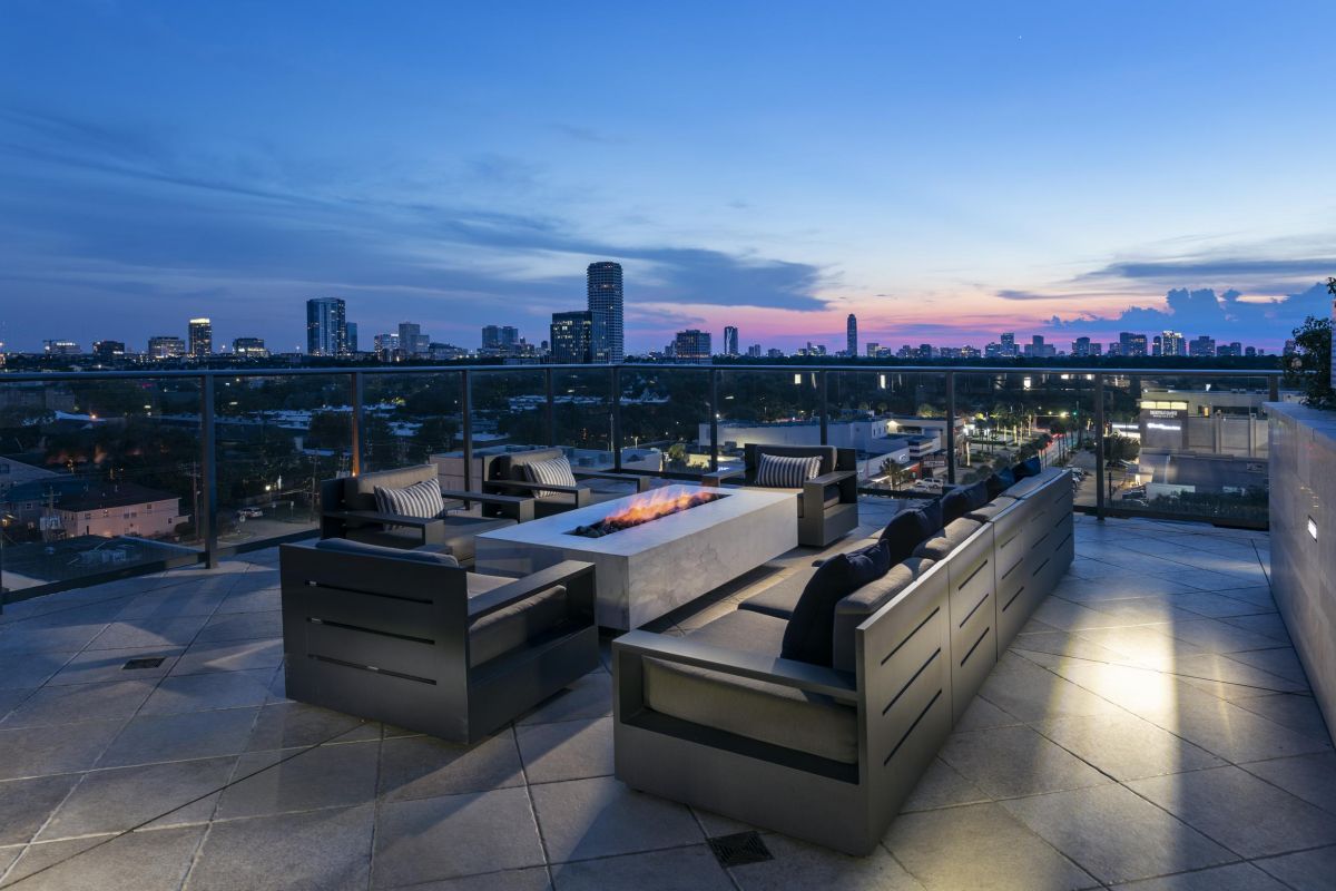 Rooftop patio at sunset with modern seating around a fire pit, overlooking a city skyline.