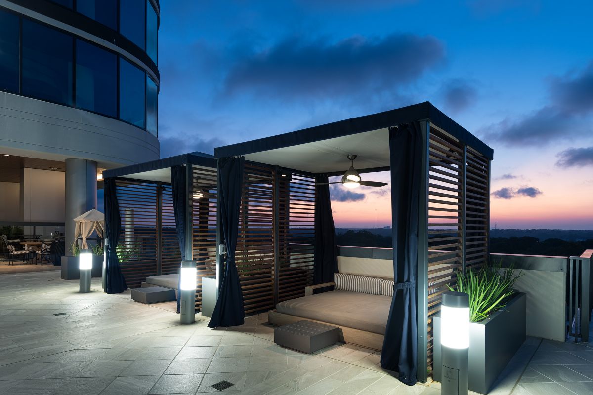 Two modern cabanas with lights and curtains on a rooftop terrace at sunset.