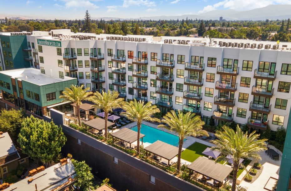 Hanover Company, Hanover Winchester Aerial view of a modern apartment complex with a central swimming pool, surrounded by palm trees and greenery.