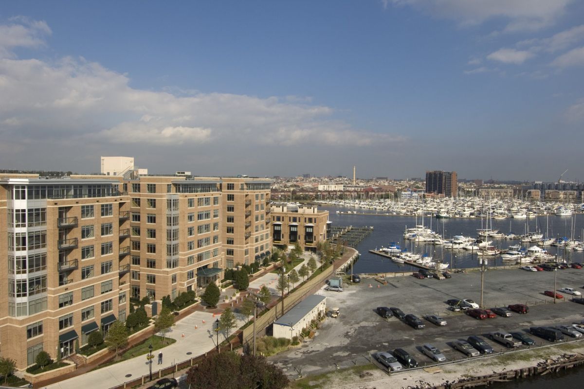 Waterfront apartment buildings overlook a marina with many docked boats and a parking lot in the foreground.