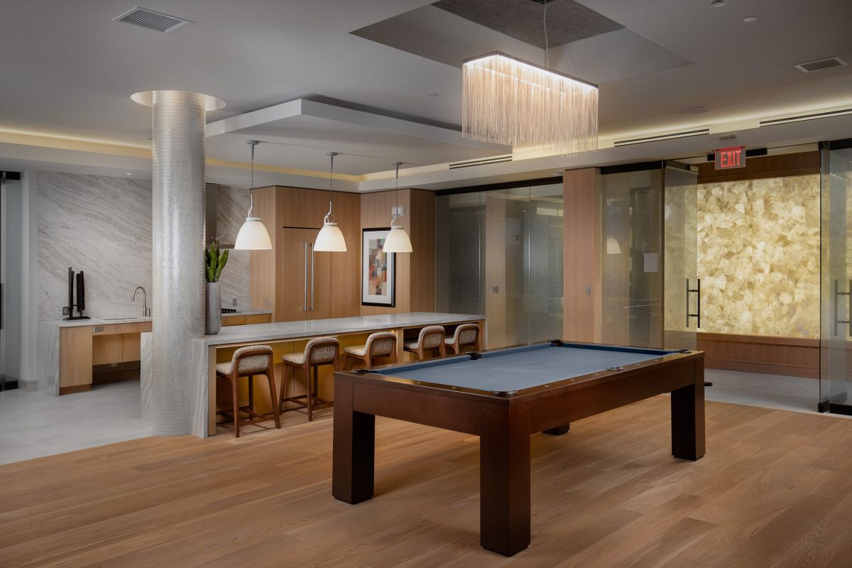 A modern lounge at Hanover Mystic River with a pool table, kitchen area, bar stools, and stylish lighting—luxury apartments redefined.