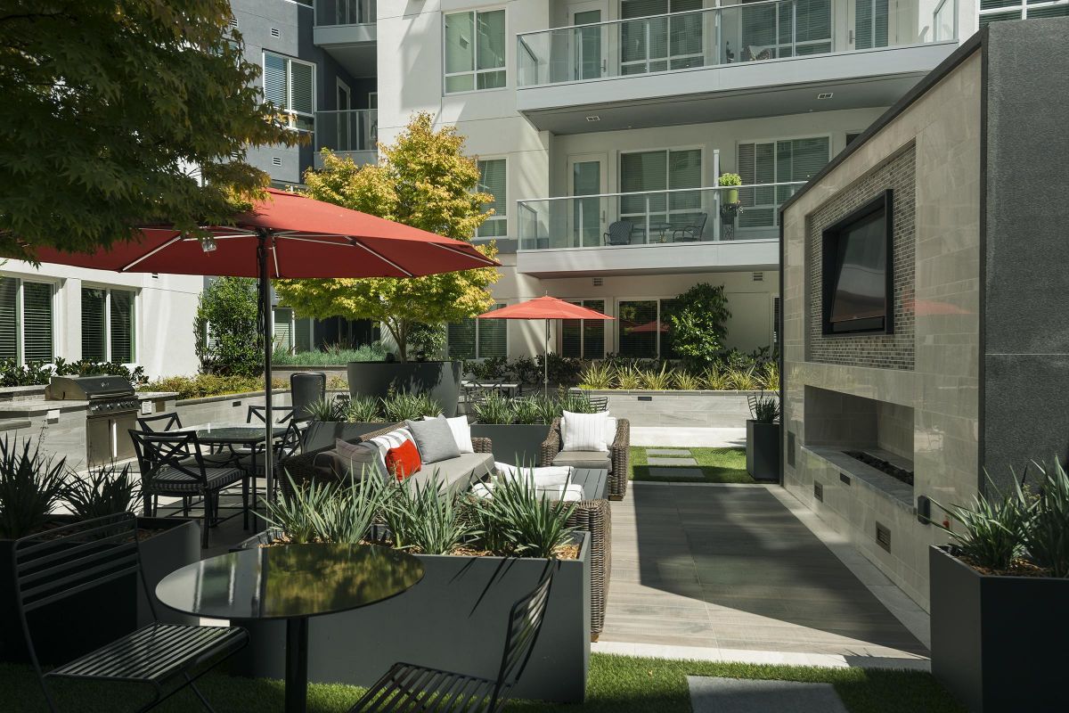 Modern outdoor patio with seating, red umbrellas, and a wall-mounted TV at an apartment complex.