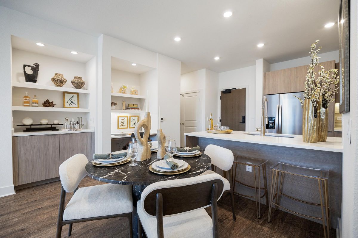 Modern kitchen and dining area with neutral decor, a round black table, and barstools at a light wood counter.