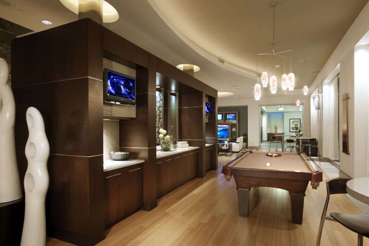 Modern lounge with a pool table, wood floors, TVs, sculptures, and stylish lighting.