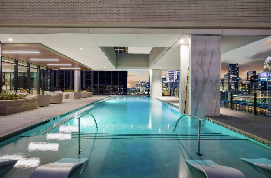 Hanover Company, Hanover Dilworth Luxurious rooftop pool area with city skyline views, featuring poolside lounge chairs and large windows.
