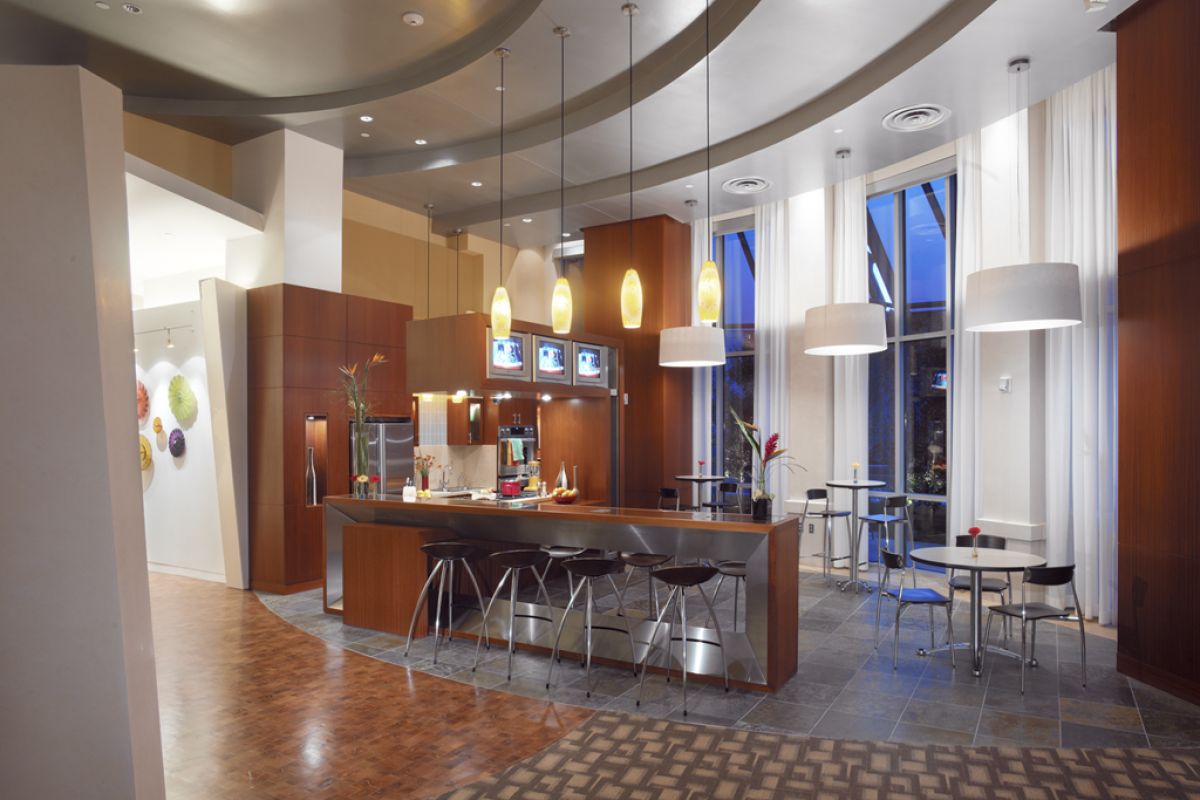 Modern lounge with pendant lights, a central island with bar stools, and small tables by tall windows.