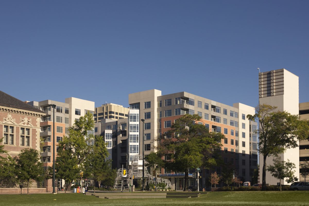 Mid-rise modern apartment buildings with trees and a grassy field under a clear blue sky.