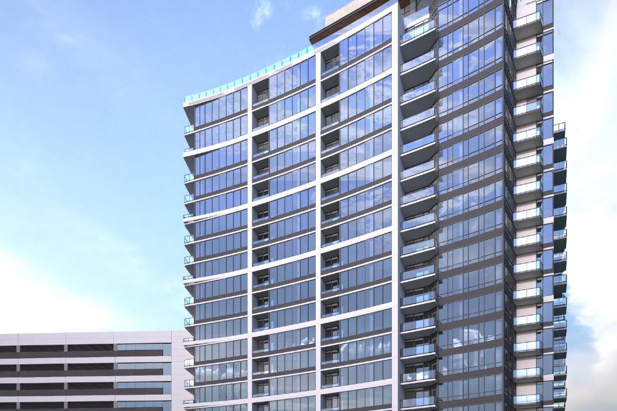 Tall modern glass building with multiple balconies against a clear blue sky, adjacent to a low-rise structure.