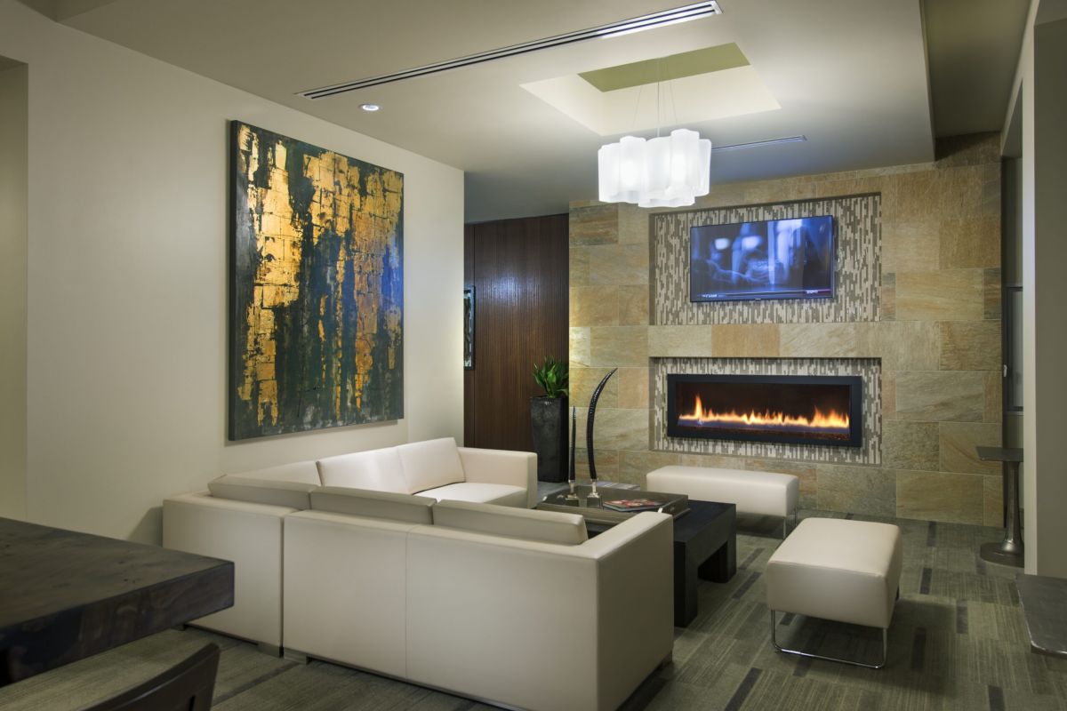Modern living room with beige sofas, abstract art, wall-mounted TV, and a lit linear fireplace.