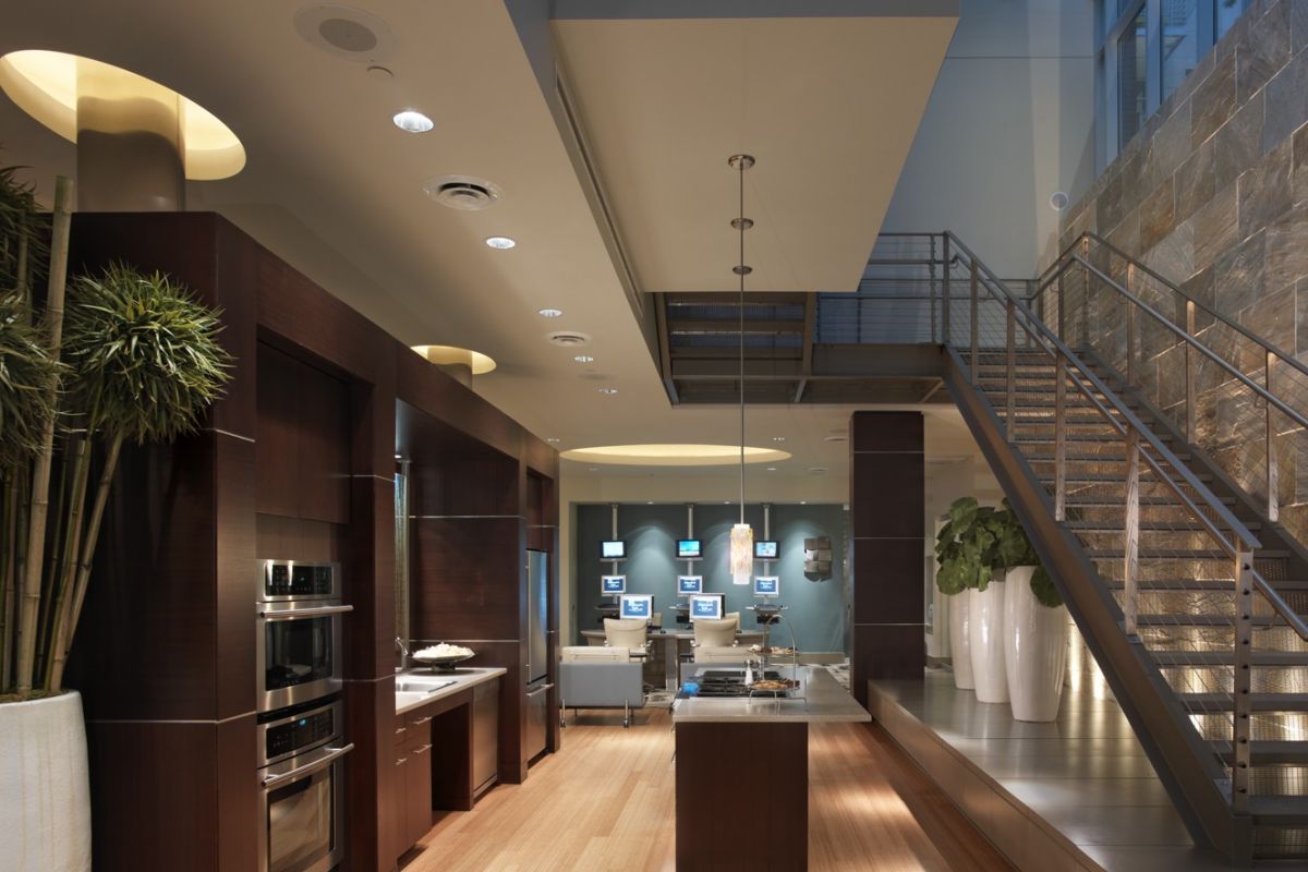 Modern kitchen with wood floors, high ceiling, glass roof, and a staircase with metal railings and potted plants.
