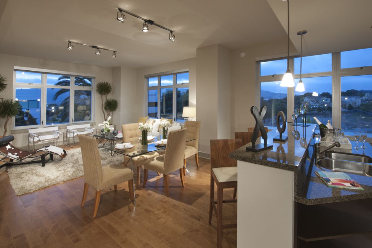 Modern open-plan living and dining area with large windows, wood floors, and contemporary Ashton Candlestick Cove decor at dusk.