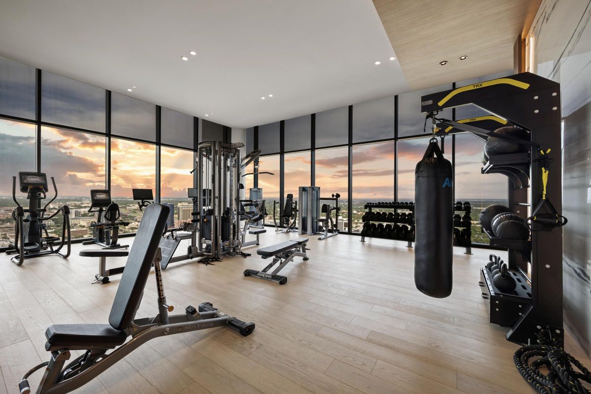 Modern gym with exercise equipment and a punching bag, overlooking a sunset through large windows.