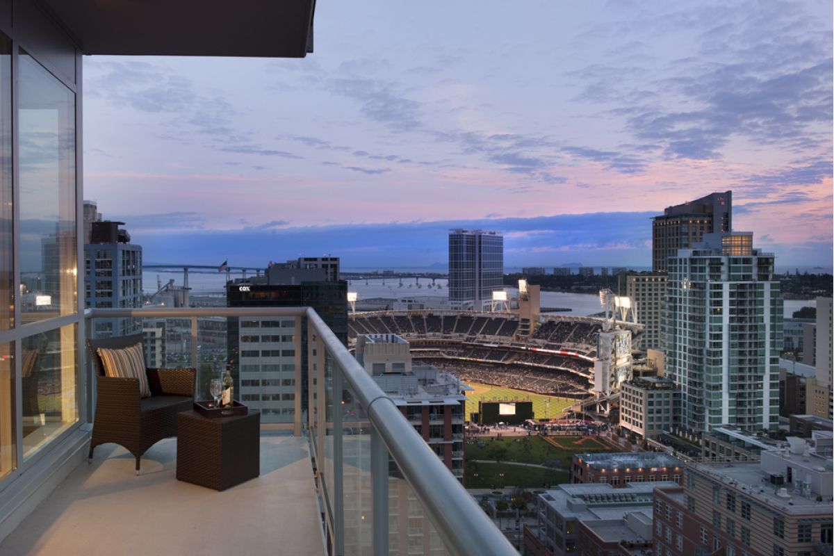 High-rise balcony with chairs overlooking a city skyline and a lit stadium at dusk.