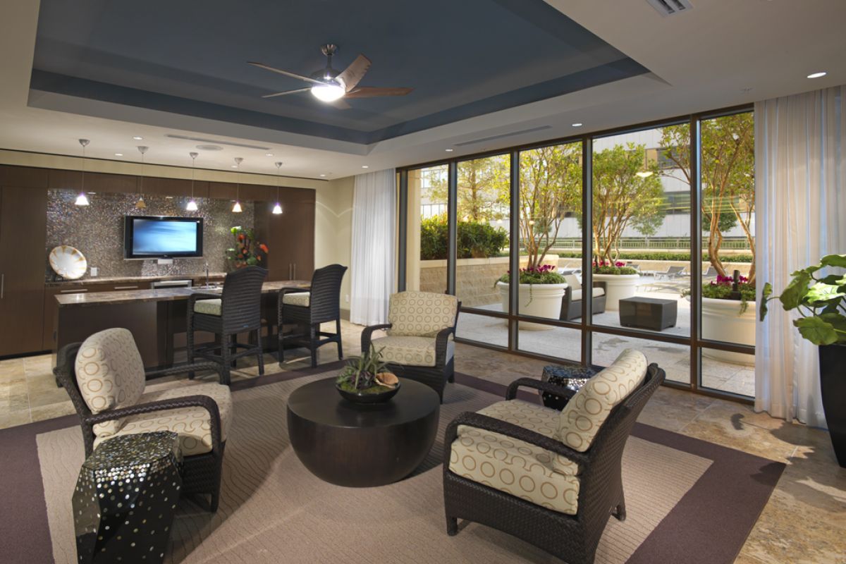 Modern lounge with armchairs, a round table, desk area, and large windows overlooking a patio with plants.