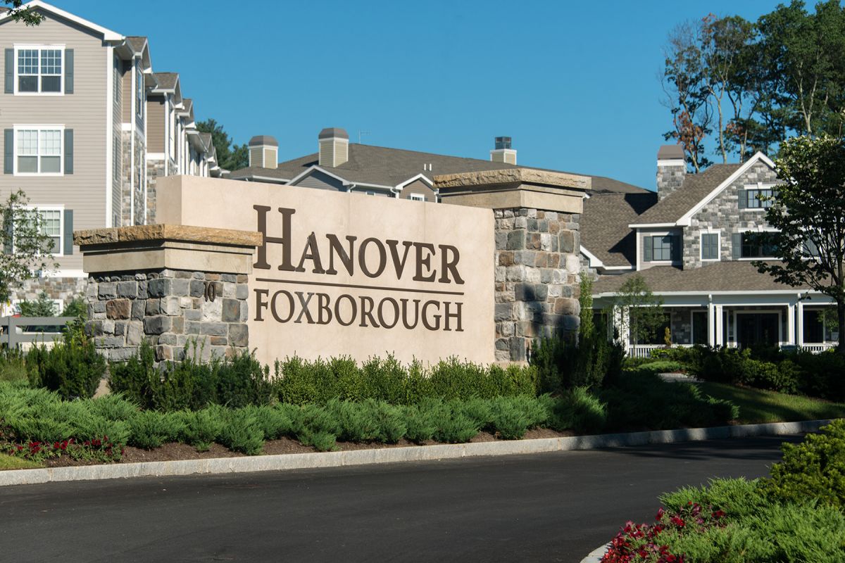 Large stone sign reads "Hanover Foxborough" in front of upscale apartment buildings and landscaped greenery.