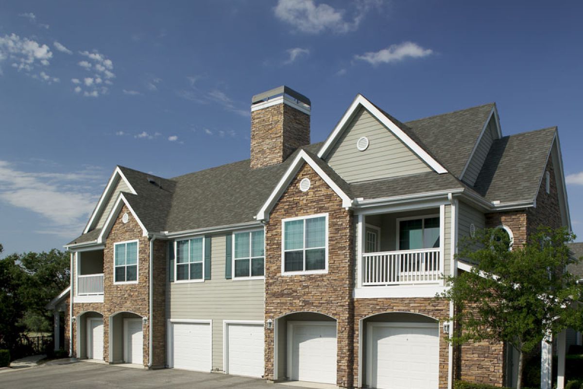 Two-story suburban townhouse with stone and siding exterior, four garages, and a small balcony under a blue sky.
