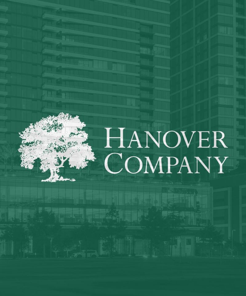 White Hanover Company logo with a tree on a green background, with buildings faintly visible behind.