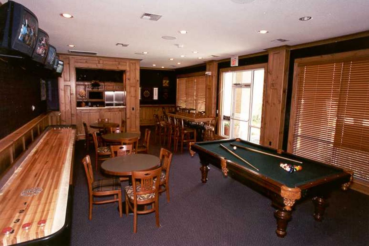 Game room at Churchill on the Park with a pool table, shuffleboard, round tables, chairs, and TVs—your Dallas apartments retreat.