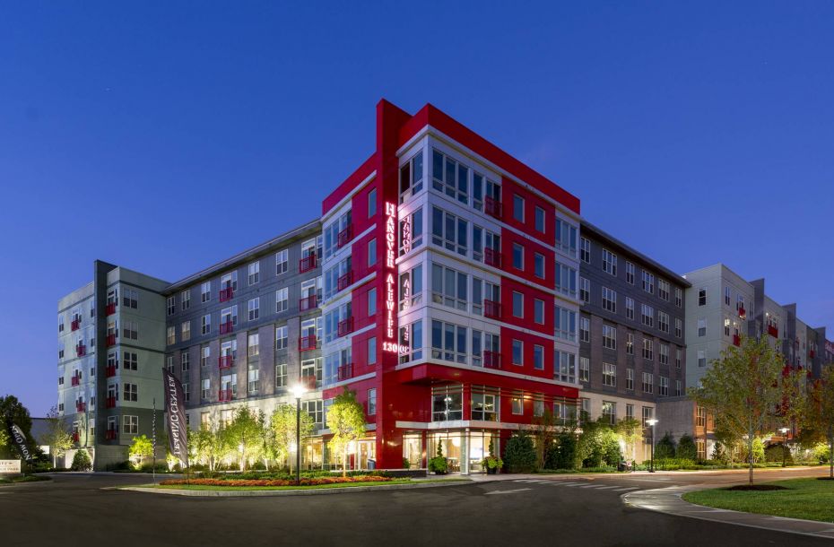 Hanover Company, Hanover Alewife Modern multi-story apartment building with red accents, surrounded by trees, at dusk.