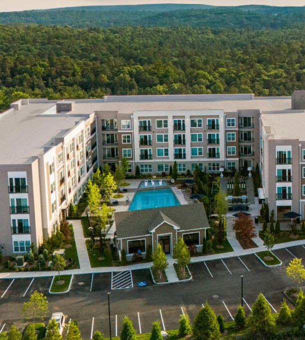 Aerial view of a modern apartment complex with a central swimming pool and surrounding trees.