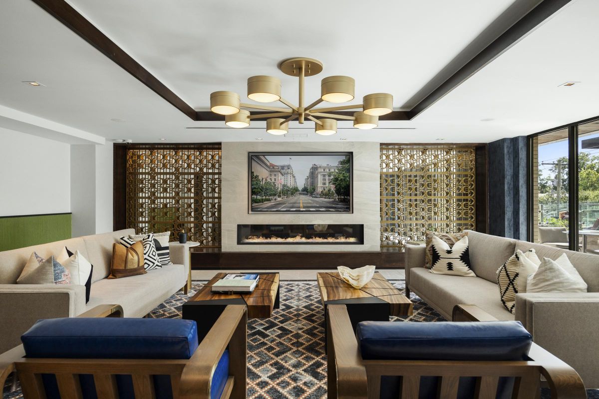 Modern living room with geometric patterns, beige sofas, blue armchairs, and a wall-mounted TV above a fireplace.
