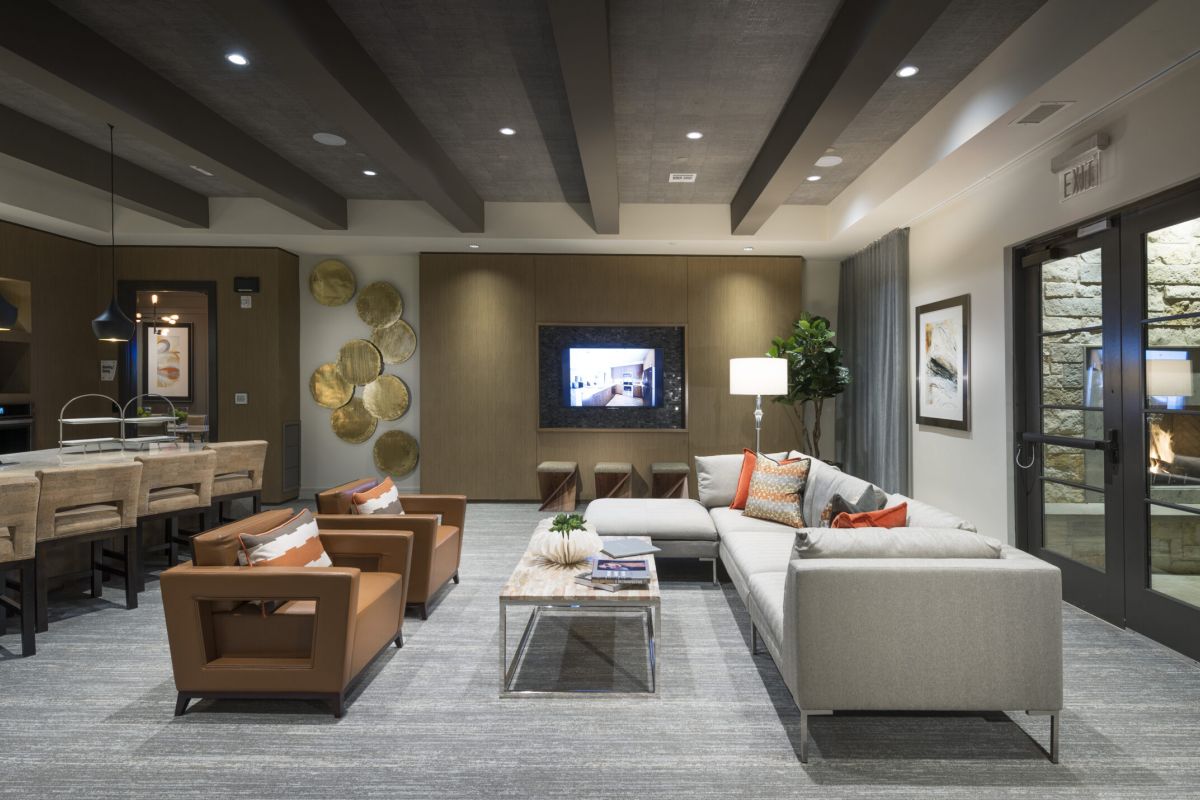 Modern living room with a gray sectional, brown chairs, TV, bar area, and glass doors to a patio with a fireplace.
