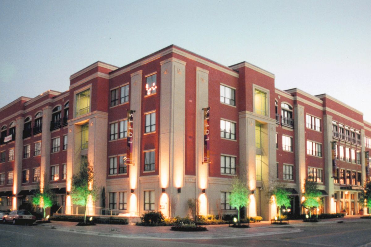 A large, modern apartment building with red and beige exterior, lit up at dusk.