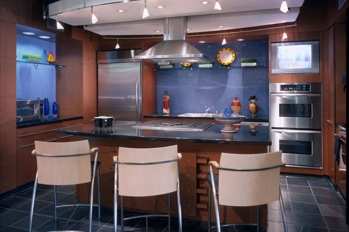 Modern kitchen with a large island, three stools, stainless appliances, and blue tile backsplash.
